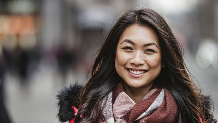 Portrait of attractive and happy smiling young Asian woman looking to camera on the street - Powered by Adobe