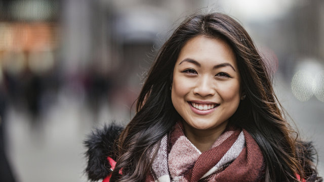 Portrait of attractive and happy smiling young Asian woman looking to camera on the street