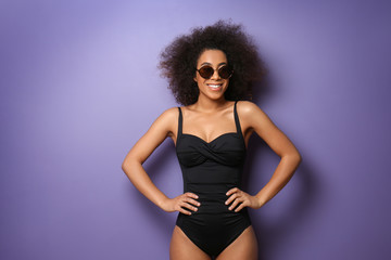 Beautiful African-American woman in swimming suit and with sunglasses on color background