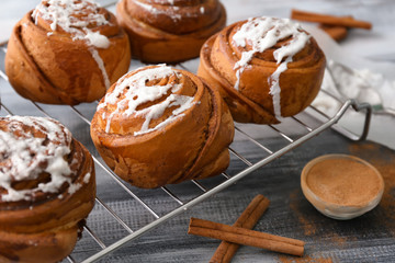 Cooling rack with delicious cinnamon buns on wooden background, closeup