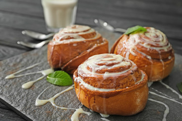 Tasty cinnamon buns with glaze on slate plate, closeup