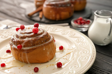 Tasty cinnamon bun with glaze and berries on plate, closeup