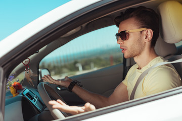 New car. Handsome man wearing sunglasses feeling really confused while driving new car