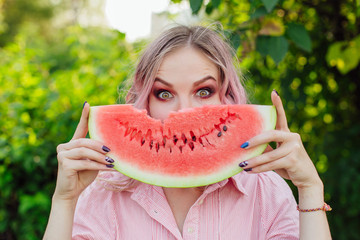 Beautiful young woman with pink hair holding juicy watermelon close to the face