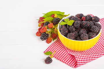 Ripe blackberries with leaves in a yellow modern bowl on a wooden board on a light background