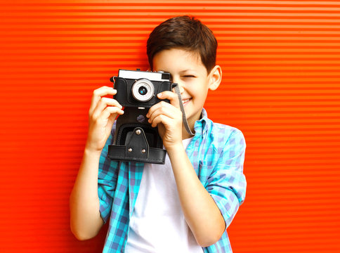 Portrait happy little boy teenager with retro camera on red background
