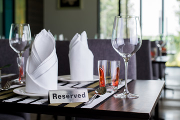 Reserved sign on a table in restaurant. Empty glasses set in restaurant
