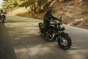 Man riding a black classic American motorcycle on the road in the mountains. Vintage effect.