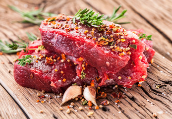 Beef steaks with seasonings on the wooden table.