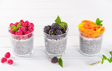 Food and drink, healthy eating and dieting concept. Homemade white chia pudding with fresh berries and green leaves for breakfast. Three glasses, raspberry, blackberry, apricot or peach.