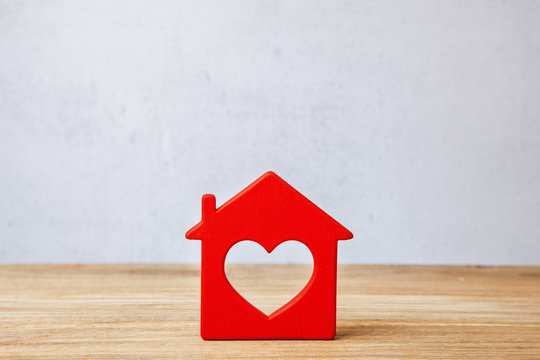 Red House with heart, sweet home. Symbol of house on wooden wall on gray wall background