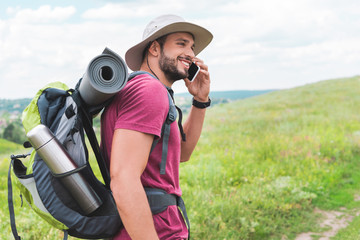 traveler with backpack talking on smartphone on green meadow