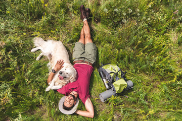 top view of tourist and golden retriever dog lying on green grass with backpack