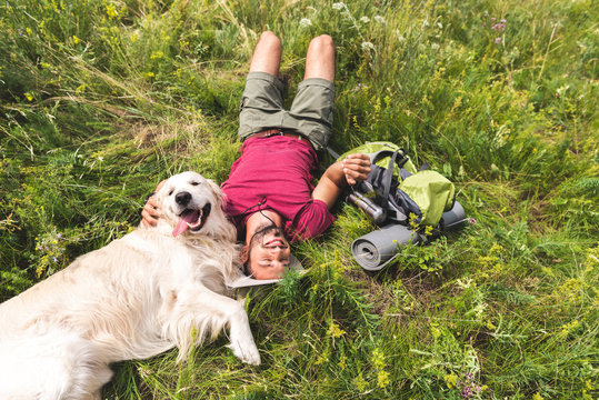 top view of happy tourist and golden retriever dog lying on green grass