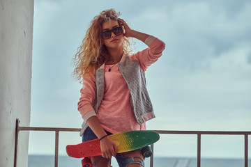 Portrait of a sensual young girl with blonde hair in sunglasses dressed in a pink jacket standing...