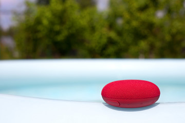 Red wireless speaker lying around the pool.