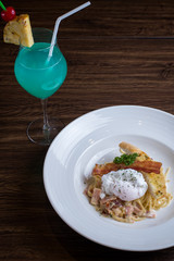 Pasta with bacon and egg yolk on a white plate on wood background. Spaghetti with stir-fried  topped fried egg.