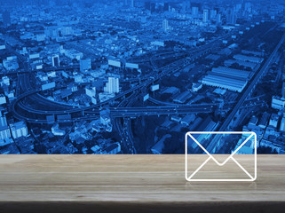 Mail icon on wooden table over modern city tower, street, expressway and skyscraper, Bangkok, Thailand, Contact us concept