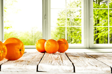 Fresh orange fruits on white wooden table and free space for your bottle or glass. Window background with summer garden landscape. 