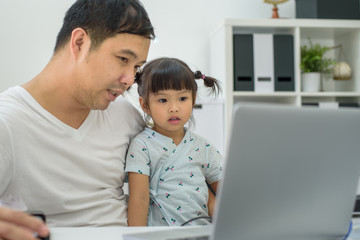 Man holding the kid  at the laptop, dad hugs a daughter, Asian family using the computer, Happy kid is smiling, Teaches his daughter to work with laptop. father and daughter looking at laptop at home