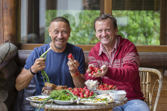 Two adult men have breakfast on the terrace with fruits from their own garden, Ukraine