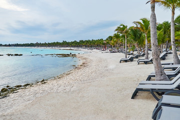The sunlight reflection on the sea in caribean ocean lagoon, the beautiful beach with long white sand at Cancun, Mexico. The deck chairs for sunbathe line-up along the coconut palm trees