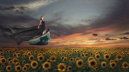 Fantasy portrait of young woman in black dress on the boat over sunflowers field