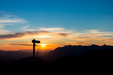 Wooden arrow pointing at colorful sunset among mountains
