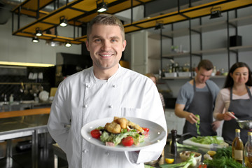 Handsome male chef holding plate with prepared dish during cooking classes