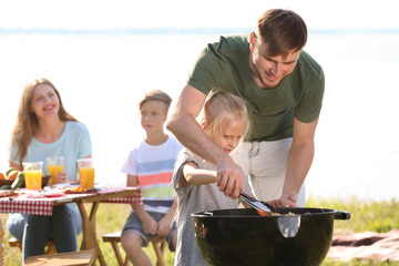 Young man with daughter cooking tasty food on barbecue grill outdoors. Family picnic