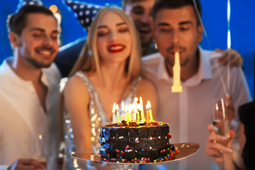 Young woman with tasty cake and her friends at birthday party in club