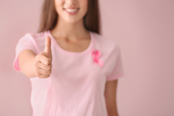Beautiful woman with pink ribbon showing thumb-up gesture on color background. Breast cancer concept