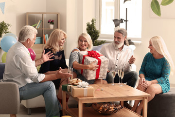 Mature woman with gift box and her friends celebrating birthday indoors