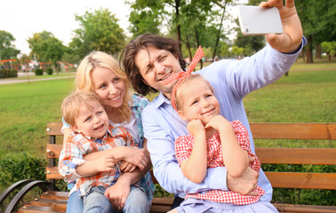 Happy family taking selfie while sitting on bench in park