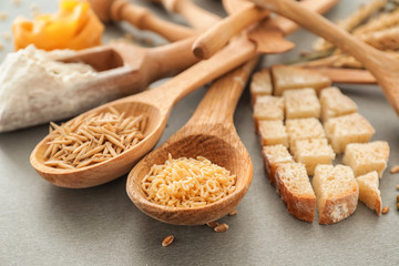 Spoons with oat grains, pasta and cut bread on grey background