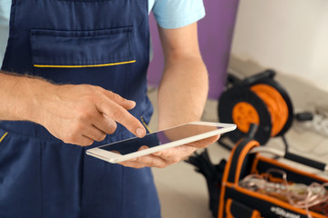 Electrician with tablet PC near distribution board indoors