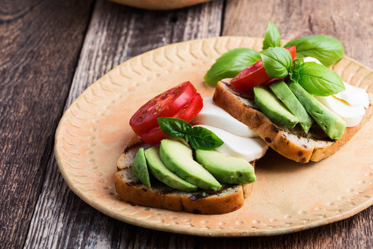 Caprese salad style toasts with avocado on  ceramic plate