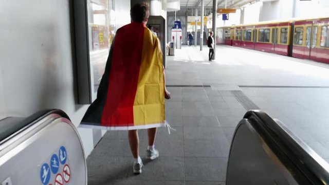 Tracking shot of a guy with a German flag around his back, running down stairs.