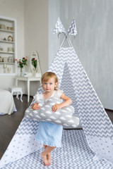 Little beautiful girl with pillow standing in teepee at nursery room.