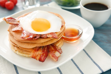 Plate with tasty pancakes, fried egg and bacon on table, closeup
