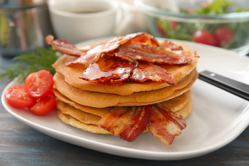 Plate with tasty pancakes and bacon on table, closeup