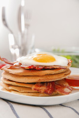 Plate with tasty pancakes, fried egg and bacon on table