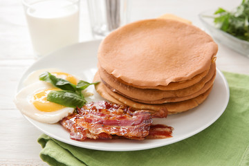 Plate with tasty pancakes, fried egg and bacon on wooden table