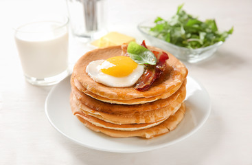Plate with tasty pancakes, fried egg and bacon on wooden table