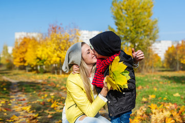 Mother and boy walking in autumn park. The child gently hugs and kisses mom.