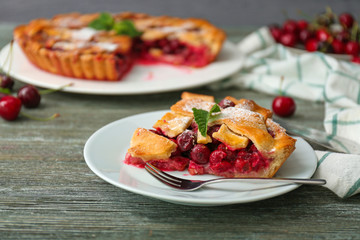 Plate with piece of delicious cherry pie on wooden table