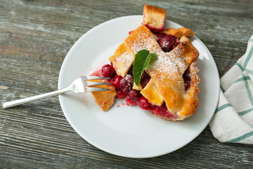 Plate with piece of delicious cherry pie on wooden table