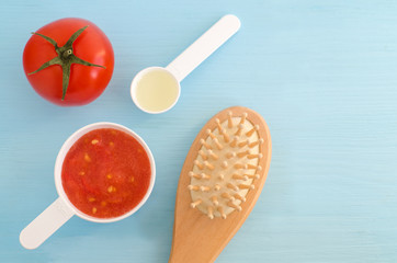Plastic scoops with tomato puree, olive oil and wooder hair brush. Ingredients for preparing homemade hair mask. DIY cosmetics recipe. Top view, copy space.