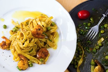 Italian pasta with shrimps on plate and rounded pan.