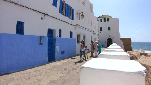 Woman with yellow dress and hat walking on the wall of Ashila in Morocco  overlooking the sea